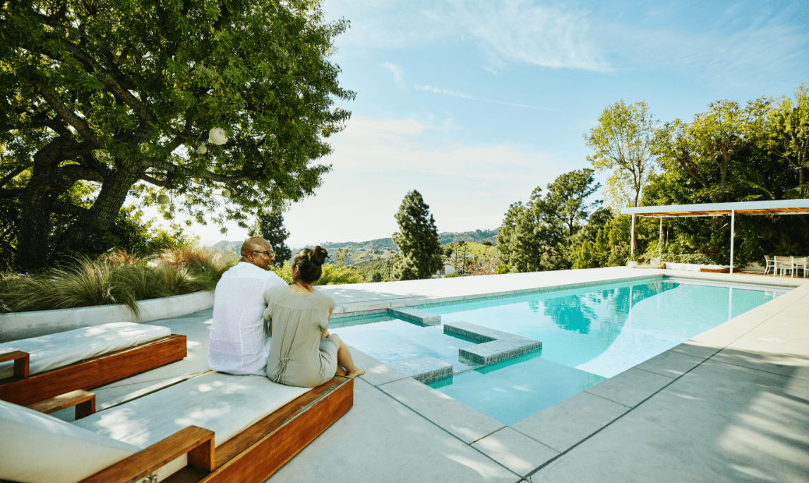 Two people sitting in casual clothing overlooking a pool in their backyard 